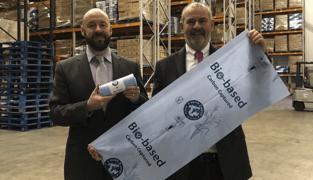 Two directors, Myles Thorn and Adam Thorn, from earth2earth and Thorn Environmental, respectively, stand in a warehouse. They are in suits and are proudly presenting their new innovation: Bio-based Carbon Captured light blue sacks.